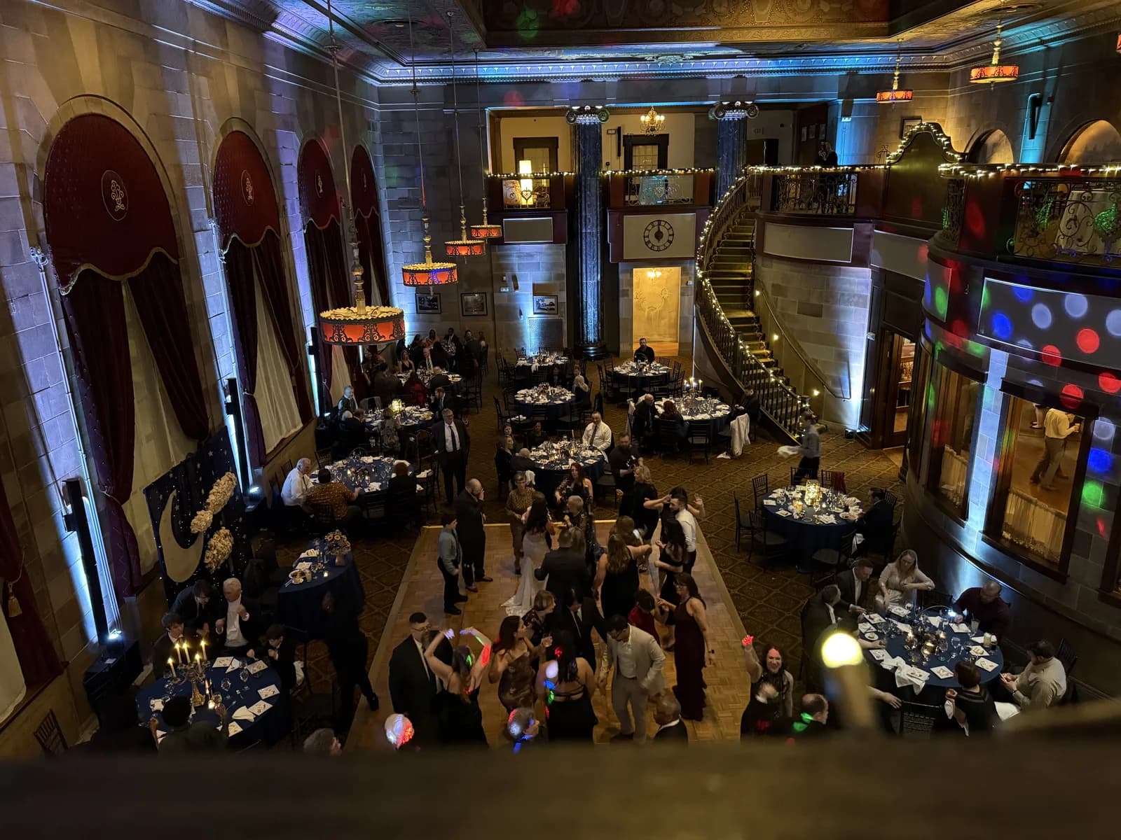 A&B Entertainment-hosted reception in a vaulted historic ballroom — colored DJ uplighting, full dance floor, navy linens on round tables